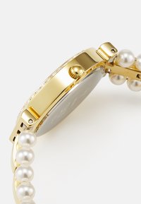 Gold-tone watch with a pearl bracelet, a round face, and a textured push-button crown. Features a crystal-accented bezel and a smooth finish.