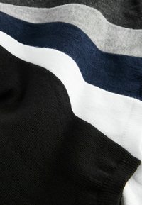 Tejidos de punto estratificados en negro, blanco, azul marino, gris claro y gris oscuro, mostrando textura y pliegues suaves.