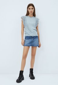 Camiseta gris claro con mangas terminadas en encaje, combinada con una falda corta de mezclilla y botas de tobillo negras con cordones. Fondo plano.
