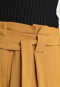 Senapsgula byxor i ett smidigt tyg, med en knytskärp i midjan och breda veck, kombinerade med en svart ribbad topp.