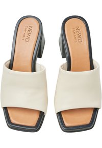 Sandali scivolati in finta pelle bianca con punta squadrata e tacco a blocco. Presentano una soletta beige con suola nera. Design semplice e moderno.