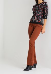 Suéter negro con un patrón y diseños florales vibrantes, combinado con pantalones acampanados color óxido y botas de tacón alto negras.