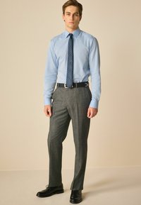 Helles blaues Hemd mit Knöpfen, marineblender gemusterte Krawatte, graue gemusterte Anzughose und schwarze Schuhe, die ein formelles Outfit präsentieren.