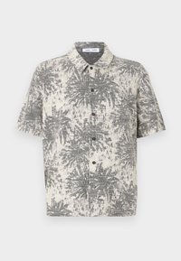 Camicia a maniche corte, con colletto, di colore crema con un motivo di palme nere, caratterizzata da un tessuto testurizzato e cinque bottoni neri sul davanti.