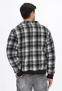 Czarna i szara kraciasta flanelowa kurtka z prążkowanym czarnym pasem w talii i mankietami, z klasycznym wzorem w szkocką kratę na miękkim materiale.