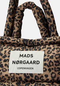Sac rembourré en imprimé léopard avec des anses torsadées et une étiquette blanche portant l'inscription « MADS NØRGAARD COPENHAGUEN » en texte noir.