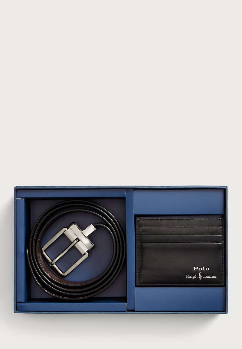 Črn usnjen pas z srebrno pravokotno sponko in usklajeno etuijem za kartice v modri darilni škatli. Etui za kartice ima štiri reže in logo.