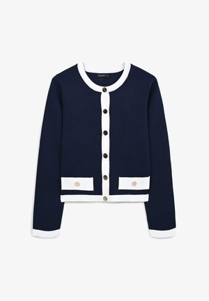 Cardigan bleu marine avec un col et des poignets blancs, doté de boutons noirs et de deux rabats de poche avec des accents clairs. Tissu tricoté texturé.