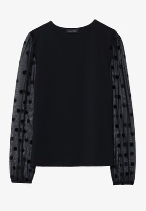 Haut noir avec un corsage en tissu opaque et des manches transparentes à pois. Présente un col rond et des poignets froncés aux manches.