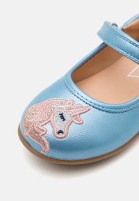 Jasnoniebieski bucik typu Mary Jane z wyszywanym na czubku różowym i srebrnym brokatowym jednorożcem oraz paskiem na górze.