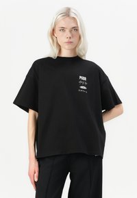 T-shirt nera oversize in cotone. Presenta maniche corte e colletto tondo. Include testo stampato bianco in vari stili sulla parte anteriore.