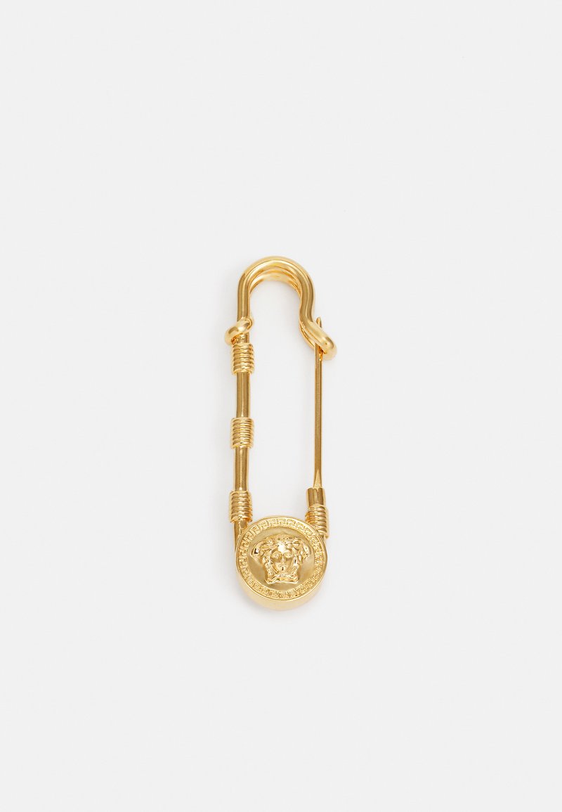 Gold safety pin with a circular Medusa head design and intricate detailing. Features coiled metal accents along the pin.