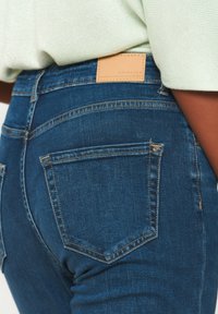 Jeans i mörkblå denim med en texturerad yta, som har bakfickor, diskreta sömmar och en beige läderetikett vid midjan.