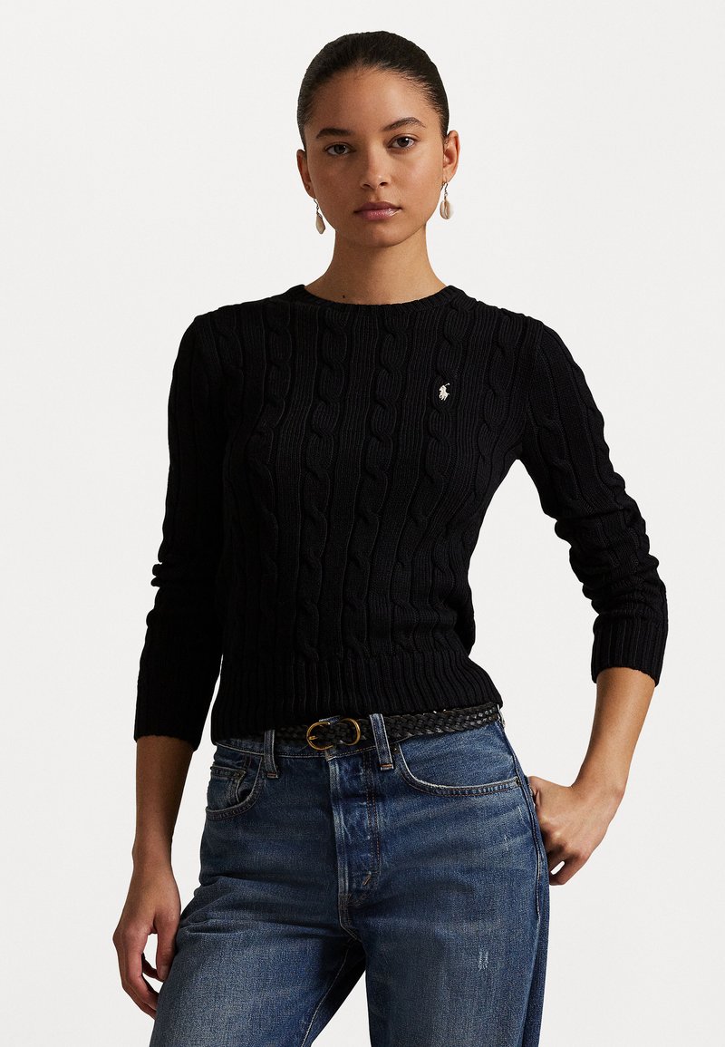 Black cable-knit sweater with round neckline and ribbed cuffs, paired with blue jeans and a woven black belt featuring a gold buckle.