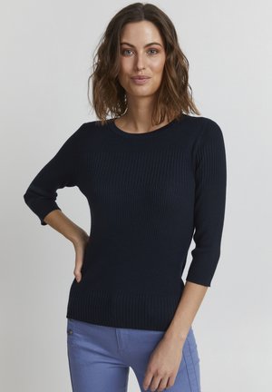 Maglione a coste blu navy con maniche a tre quarti, scollatura rotonda e finitura testurizzata, abbinato a pantaloni azzurri chiari con dettagli a bottone.