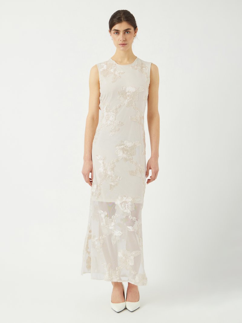Robe sans manches, longue jusqu'au sol, en beige clair avec broderies florales. Couche inférieure transparente avec des détails texturés. Chaussures à talons hauts blanches.