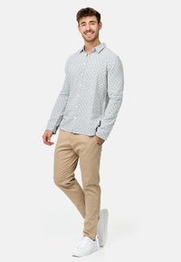 Camisa de botones azul clara con un patrón de lunares oscuros, combinada con chinos beiges y zapatillas blancas. Textura suave y diseño ajustado.
