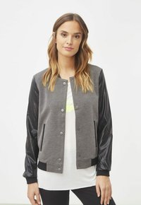 Chaqueta bomber de punto gris con mangas de piel sintética negra, cierre frontal de botones a presión, puños acanalados y bolsillos laterales. Diseño sencillo y deportivo.