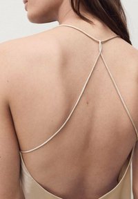 Abito beige in satin con spalline sottili e design incrociato sulla schiena, texture liscia e scollo profondo sulla schiena che mette in mostra la pelle.