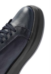 Zapatilla de cuero azul oscuro con un acabado suave, punta redonda, suela de goma negra texturizada y cordones tonalizados. Presenta un diseño de suela en capas.