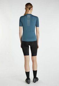 Korte mouw fietsshirt in teal met een gestructureerd patroon en reflecterende accenten, gecombineerd met zwarte gepaddingde fietsbroek en fietsschoenen.