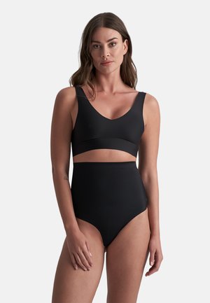 Femme portant un short taille haute sans coutures noir et un crop top à larges bretelles assorti sur un fond blanc uni.