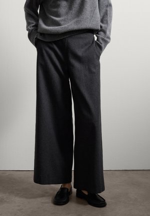Pantalons à jambes larges, de couleur gris foncé, en tissu doux, présentant une coupe décontractée et des poches avant, associés à des mocassins noirs.