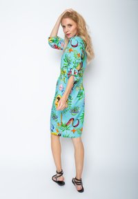 Hellblaues Kleid mit bunten, verspielten Mustern, kurzen Puffärmeln und knielangem Schnitt, kombiniert mit schwarzen Sandalen.