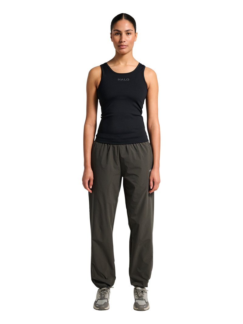 Femme debout, face à l'avant, portant un haut noir sans manches, un pantalon ample gris foncé et des baskets grises sur fond blanc.