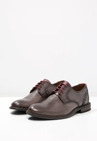 Scarpe in pelle grigia con una finitura liscia, caratterizzate da un design lacciato bordeaux, punta rotonda e cuciture a contrasto lungo i lati.