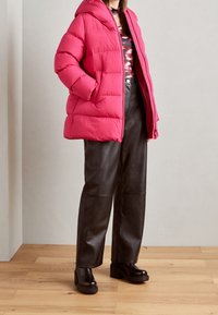 Chaqueta acolchada rosa con capucha, combinada con pantalones de cuero negros de cintura alta y botas negras gruesas con plataforma.