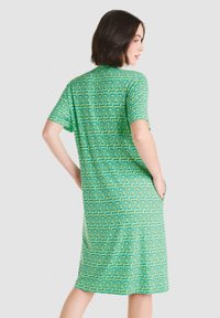 Vestido verde de manga corta con un patrón geométrico de triángulos en verde más oscuro. Tiene un corte relajado y bolsillos laterales. Textura de tela suave.