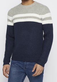 Maglione lavorato a maglia con strisce orizzontali grigie, bianche e navy. Collo rotondo, polsini e bordo a costine, e tessuto testurizzato.