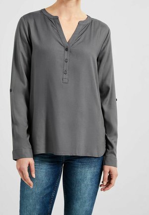 Grey long-sleeve blouse with three front buttons worn with blue jeans, shown on a person from neck to hips against a plain background.
