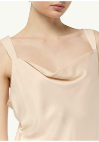 Satynowa koszulka w miękkim beżu z dekoltem w kształcie poduszki oraz cienkimi ramiączkami, o gładkiej fakturze i luźnym kroju.