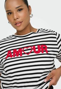 Camiseta de rayas en blanco y negro con la palabra "AMOUR" bordada en letras rojas, con un corazón en lugar de la letra "O". Tejido de algodón suave.
