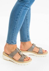 Grijze geweven sandalen met twee brede bandjes, voorzien van metalen accenten en een chunky witte zool. Gecombineerd met blauwe skinny jeans.