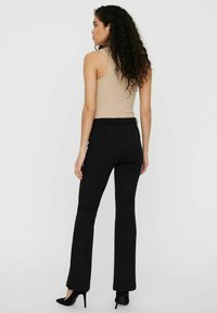 Pantalons évasés noirs au toucher lisse, dotés d'une taille ajustée et d'un léger éclat. Associés à un débardeur beige.