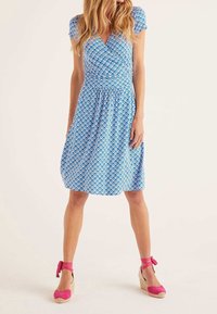 Blå omslagsklänning med vitt vågmönster, korta ärmar och figurnära midja. Kombinerad med rosa espadrillos med kilklack och ankelband.