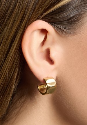 Boucles d'oreilles en or avec une finition texturée, présentant une forme moderne et courbée qui étreint partiellement le lobe de l'oreille.