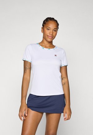En kvinne med flettet hår smiler mens hun har på seg en hvit treningsskjorte med blågrønne detaljer og en marineblå tennisskjørt, noe som viser en sporty stil.