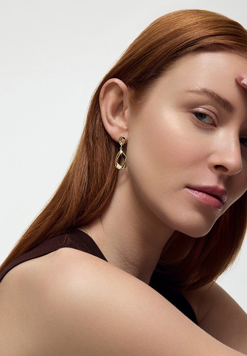 Złote długie kolczyki w kształcie abstrakcyjnym z otwartym diamentem, wyróżniają się gładkimi powierzchniami i wypolerowanym wykończeniem.