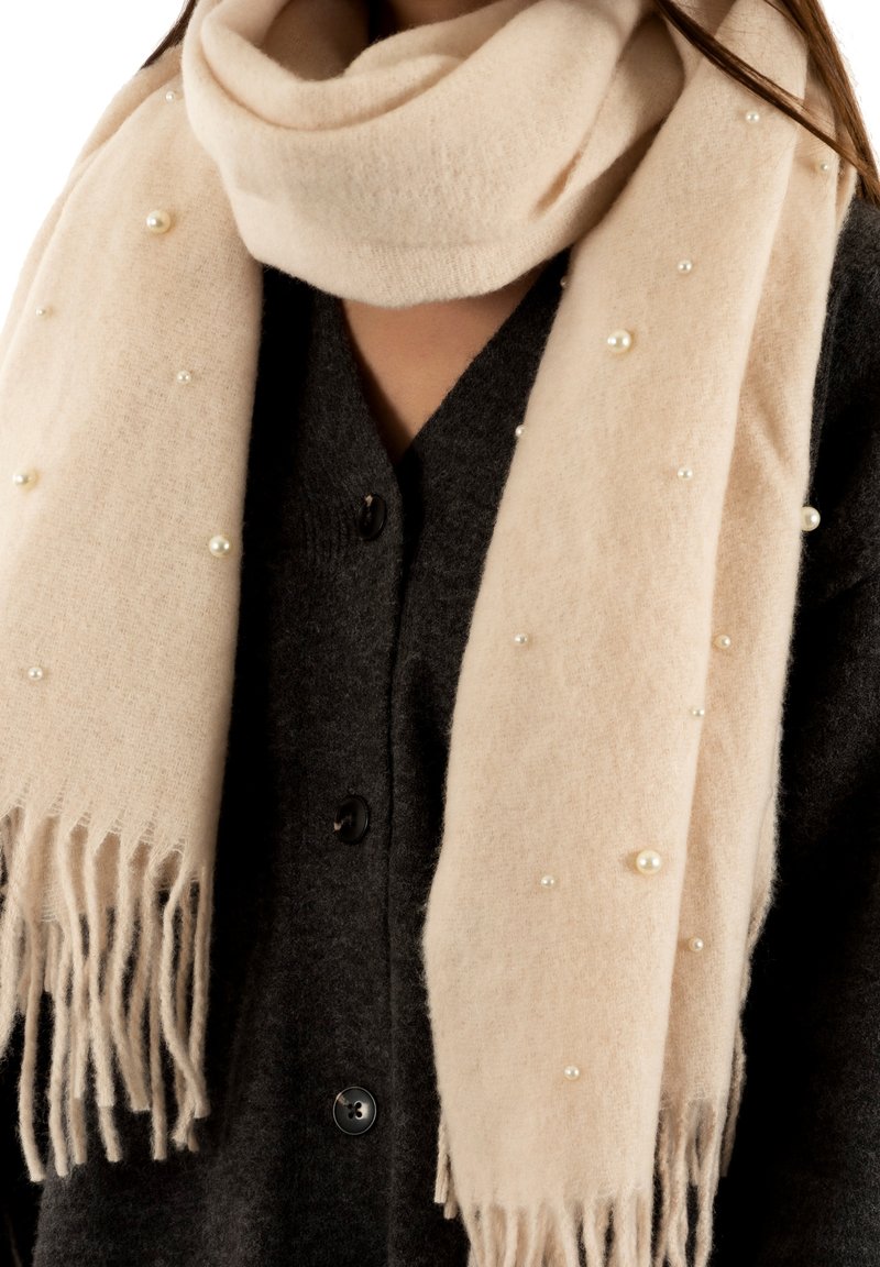 Écharpe beige au toucher doux, ornée de petites perles en différentes tailles, et finition avec des bords frangés.
