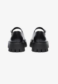 Black leather shoes with a chunky, ridged sole and an ankle strap. The design features a smooth texture and a narrow buckle accent.