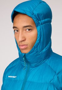 Blue insulated jacket with a high collar and hood. Features quilted texture, zip closure, and a logo on the chest. Smooth, shiny fabric.