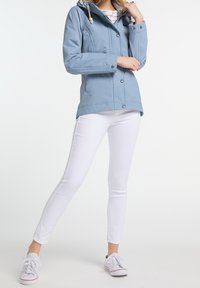 Ljusblå jacka med huva, knäppning med knappar och två sidofickor. Matchad med vita tajta jeans och vita sneakers.