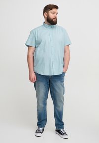 Cămașă bleu deschis cu mânecă scurtă, cu nasturi, croi lejer, asortată cu blugi denim de nuanță medie și adidași negri. Stil simplu, casual.
