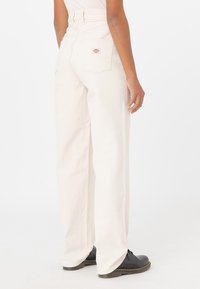Pantalones anchos y blancos de cintura alta, hechos de una tela resistente. Presentan bolsillos traseros y una pequeña etiqueta de la marca cerca del bolsillo derecho.