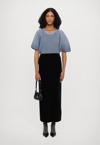 Helles blaues, geripptes Strickoberteil mit kurzen Puffärmeln, kombiniert mit einem langen schwarzen Samtrock. Schwarze Handtasche mit einem runden Akzent. Schwarze spitze Absatzschuhe.