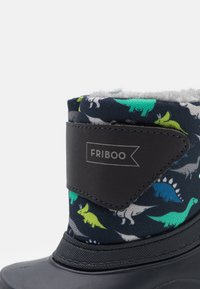 Bota de goma negra con un suave interior gris. La parte superior es de tela azul marina con coloridos patrones de dinosaurios y una correa ajustable negra.